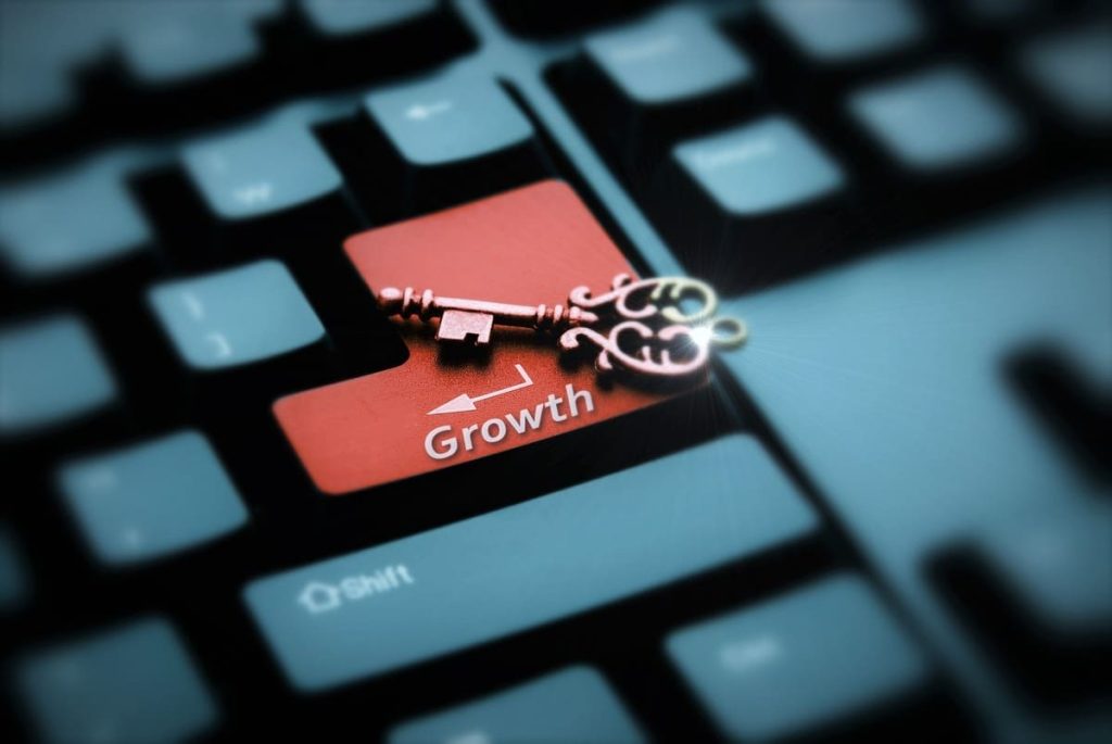 Primer plano de un teclado de computadora oscuro donde destaca la tecla "Enter" en color rojo con la palabra "Growth" (Crecimiento). Sobre ella descansa una llave antigua de metal labrado, simbolizando la tecnología como clave del éxito.